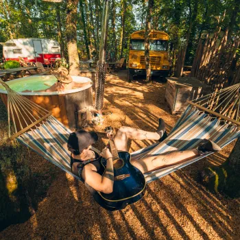 Couple relaxing in a hammock in a sunny, wooded campsite.