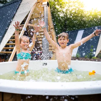 Children splashing joyfully in an outdoor hot tub, sunlight in the background.