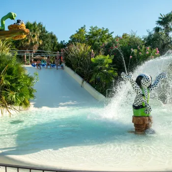 Water slide in a park, with splashing monkey statue and vibrant greenery.