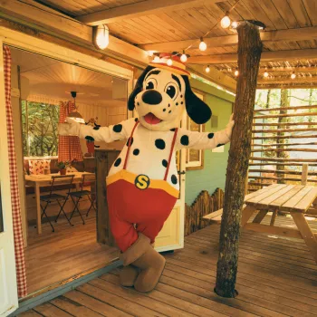 spotty in red shorts at a cozy wooden cabin entrance.