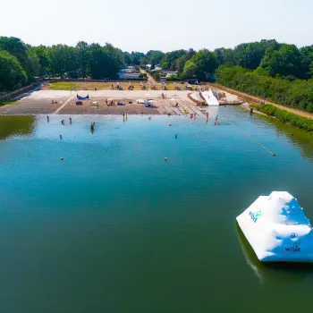 Calm lake with inflatable iceberg and sandy beach surrounded by trees.