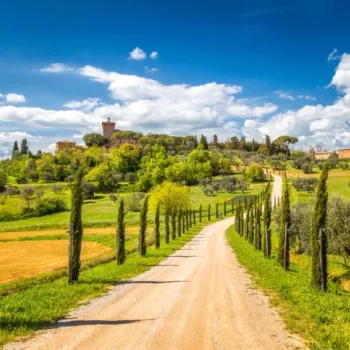 Tuscan countryside with a dirt road, cypress trees, and a scenic hilltop.