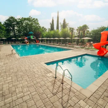 Two pools with red slides and lounge chairs under umbrellas on a sunny day.