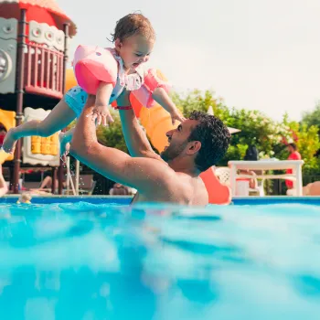 Father and child playing in a pool, surrounded by colorful playground equipment.