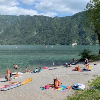 Beachgoers on a pebbly shore with green mountains in the background.