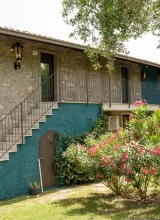 Stone building with stairs, surrounded by greenery and flowering bushes.