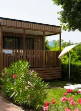 Cozy wooden cabin with a porch, surrounded by greenery and flowers; two lounge chairs nearby.