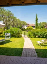 Sunny garden with lounge chairs, umbrella, and a path leading to trees and shrubs.