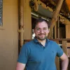Smiling man in glasses stands on wooden porch.