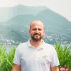 A man in a white polo shirt stands before a mountain landscape.