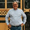 Man smiling in front of a yellow school bus.