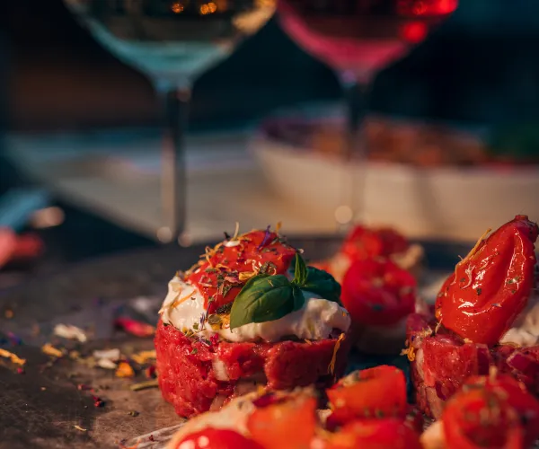 Bruschetta with cherry tomatoes and basil, two wine glasses in the background.