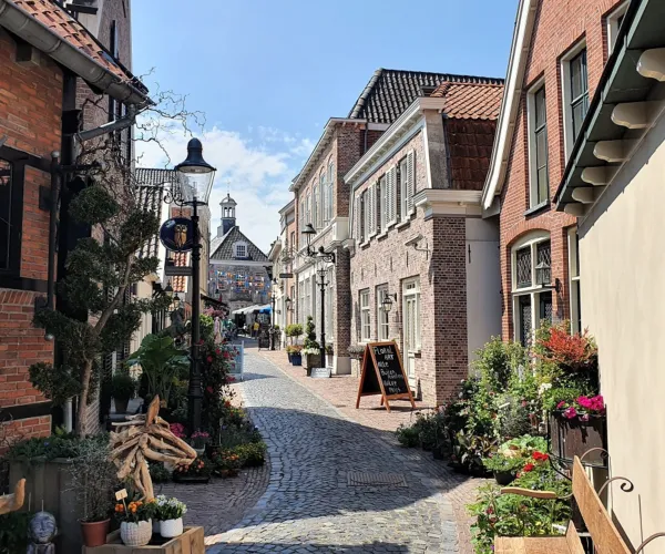 Narrow cobblestone street lined with quaint brick buildings under a clear blue sky.