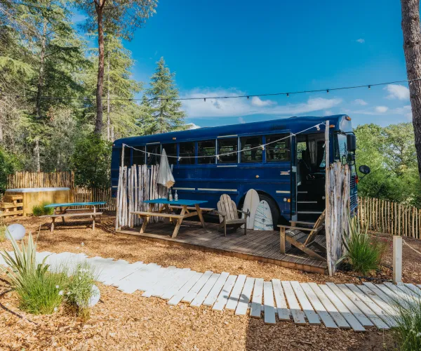 Blue bus converted into a cozy outdoor seating area in a forest setting.