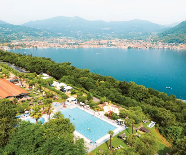Aerial view of a pool beside a lake, surrounded by trees and mountains in the distance.
