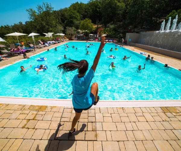 Person jumping into a busy outdoor pool on a sunny day.