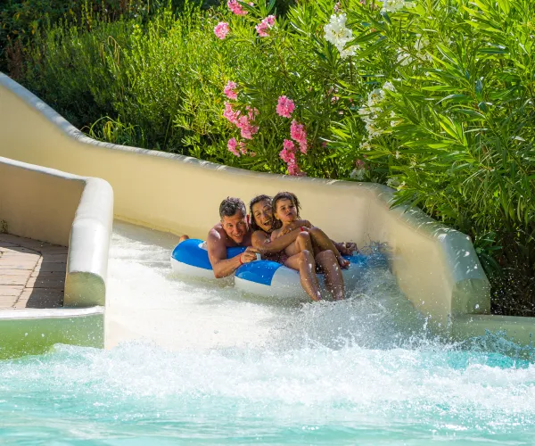 Three people in an inflatable raft slide down a water slide.