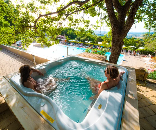 Two people relaxing in a hot tub with a scenic view of a pool and greenery.
