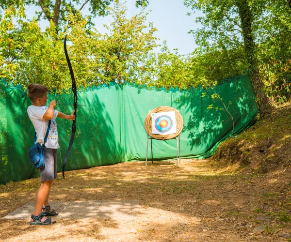 Boy aiming arrow at archery target outdoors.