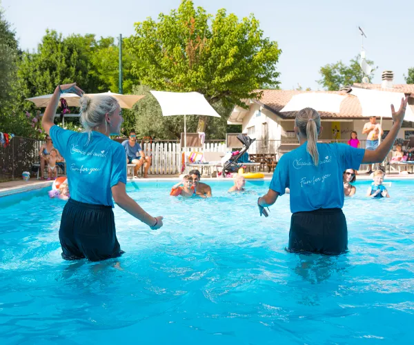 Two instructors lead a pool exercise class outdoors.