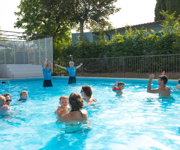 Pool swim class with adults and children, sunny day, instructors leading exercises.