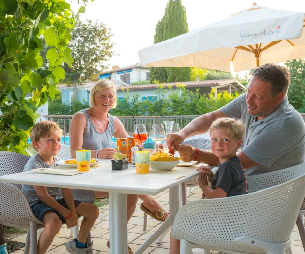 Family enjoying a meal at an outdoor restaurant, surrounded by greenery.