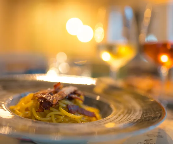 Pasta dish with wine glasses on a blurred background.
