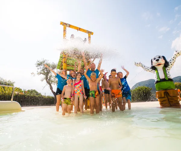 Children playing in a water park, splashing under a large bucket.