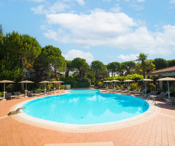 Circular pool surrounded by loungers and trees under a clear blue sky.