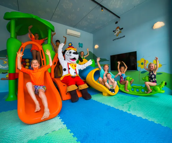Children and a mascot enjoy colorful slides indoors.