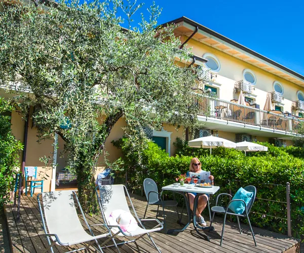 Sunny patio with chairs, table, and umbrella, near a large tree and residential building.