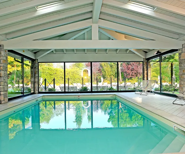 Indoor pool with large windows, surrounded by trees outside.