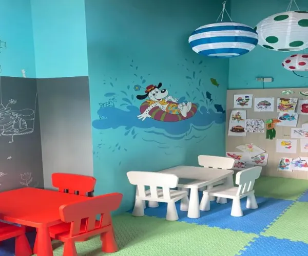 Colorful children's playroom with small tables, chairs, and playful wall murals.