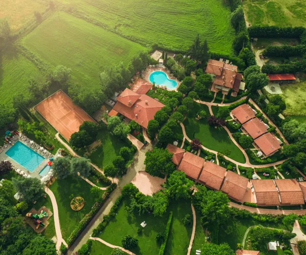 Aerial view of resort with two pools, surrounded by green fields and trees.