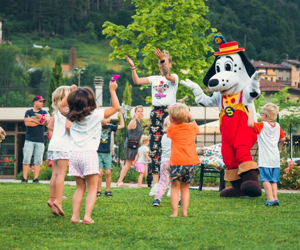 Children dancing with a costumed character in a park setting.