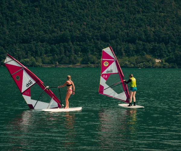 Windsurfers on a lake with forested hills in the background.