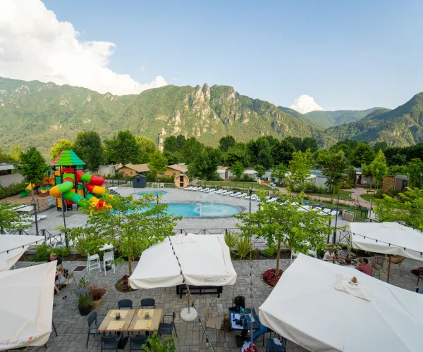 Poolside cafe with white umbrellas, colorful slides, and mountain backdrop.