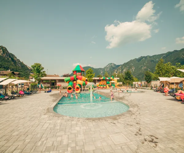 Outdoor pool with colorful slides, surrounded by mountains and loungers.