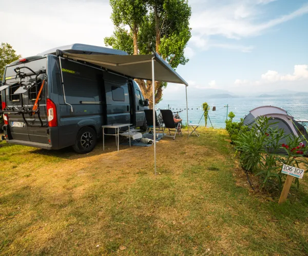 Campervan and tent on grassy lakeside campsite under clear blue sky.