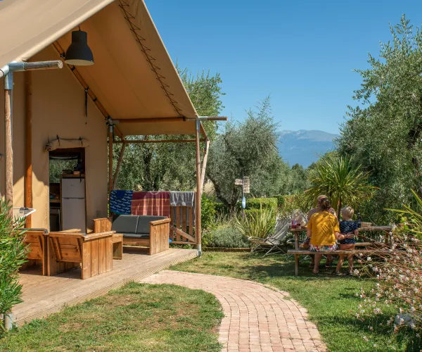 Tent with patio in sunny garden, group seated at table, distant mountains.