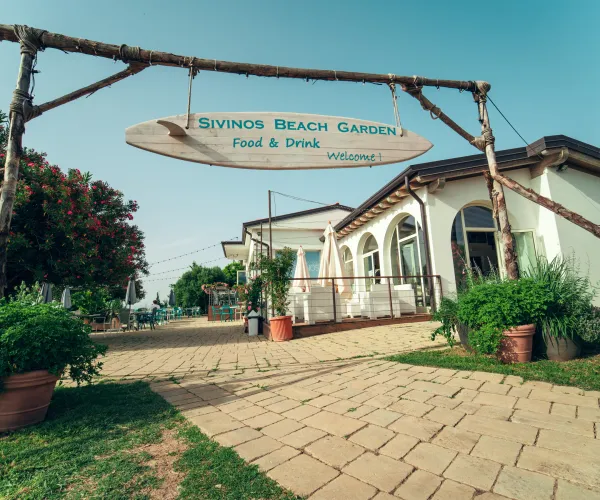 Beachside café entrance with rustic sign and lush greenery.
