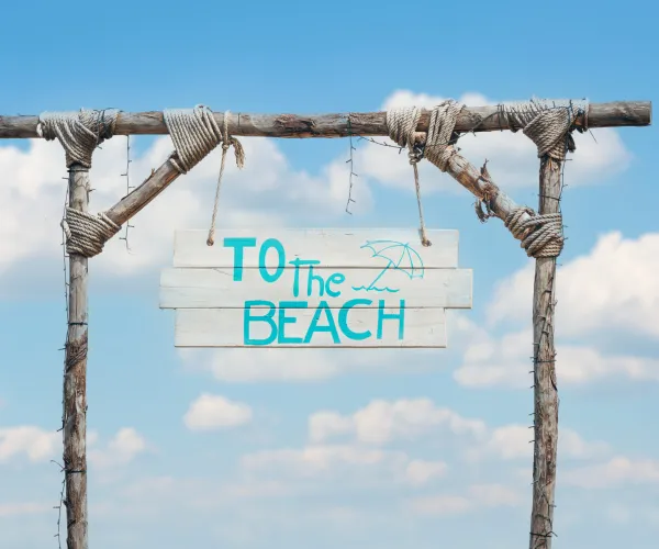 Rustic beach sign against a blue sky and clouds.