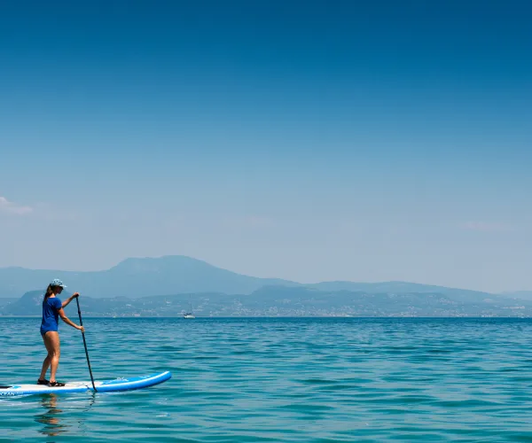 Paddleboarder on calm blue sea with distant mountains.