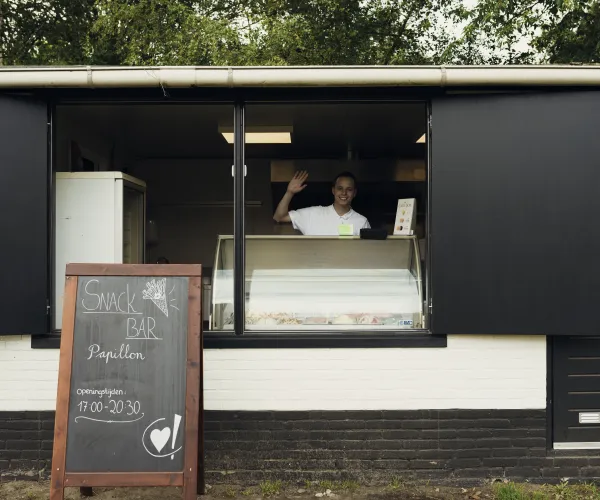 Ice cream shop with open window, person waving inside, menu board outside.