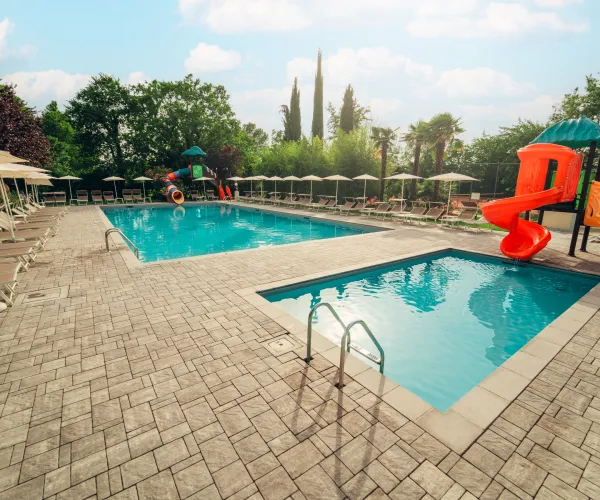 Outdoor pool with lounge chairs, surrounded by trees, and a red slide.
