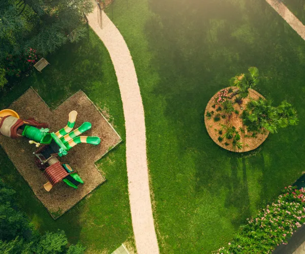 Playground with colorful dinosaur slide, surrounded by green grass and pathways.