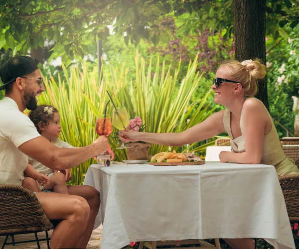 Family toasting glasses at an outdoor table under trees.
