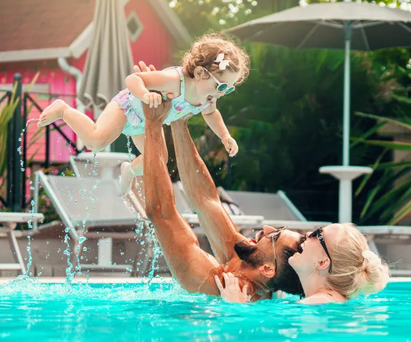 Man and woman lifting a child in a pool, with joyful expressions.