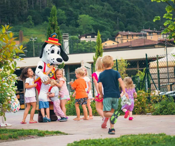 Children gather around a Dalmatian mascot in a park setting.