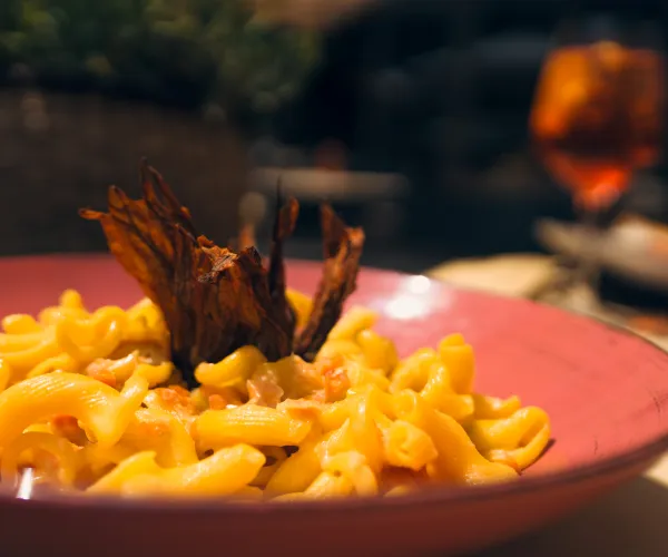 Macaroni and cheese with crispy garnish on pink plate, blurred drink in background.
